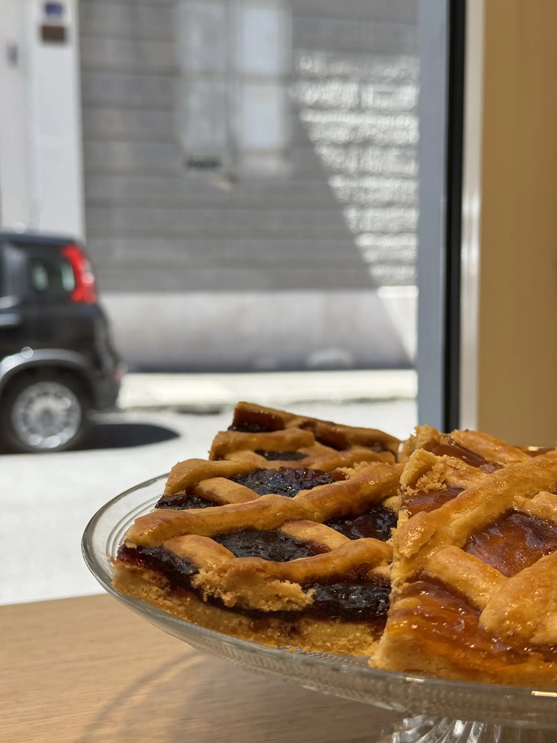 Una crostata di marmellata con la griglia di pasta frolla, su un’alzata di vetro davanti alla vetrina