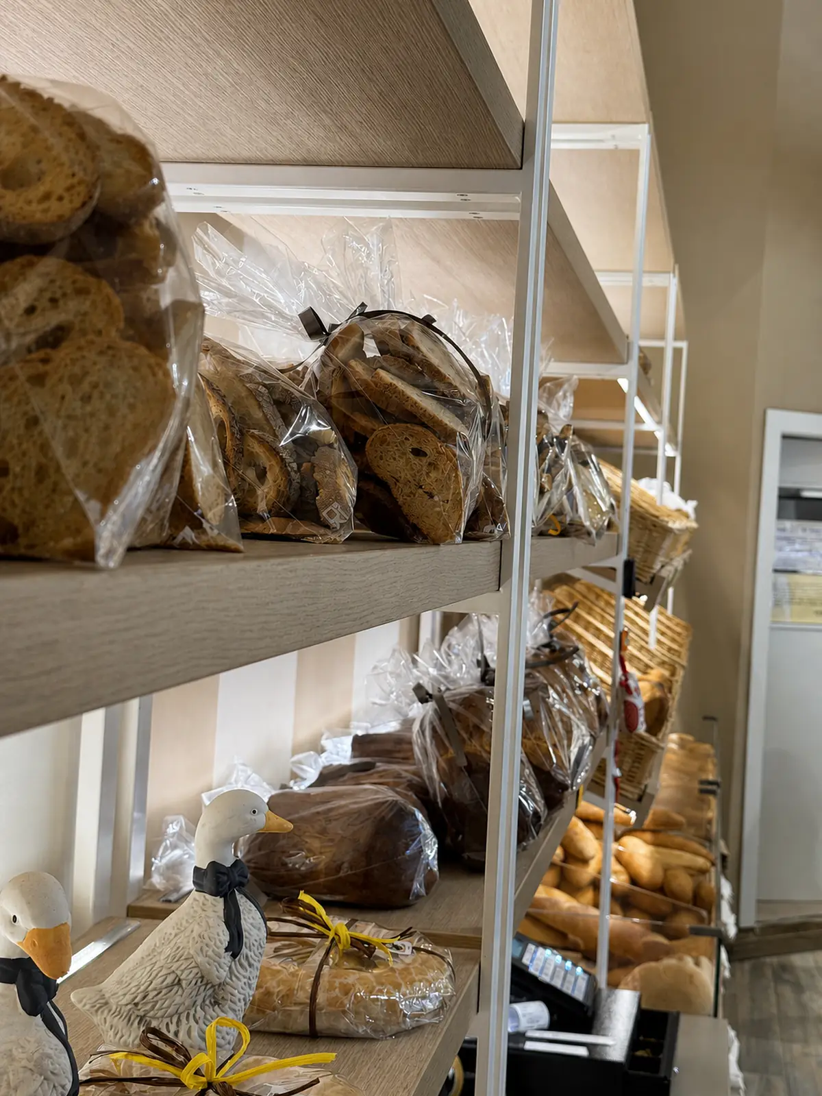 Gli scaffali di legno con il pane confezionato: pagnotte, pane a fette e i filoni nei cesti in fondo